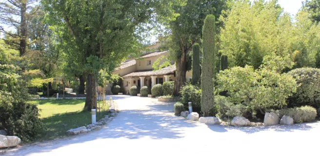 Une grande bastide provençale nichée au cœur d’un écrin de verdure, accessible par une allée ombragée.