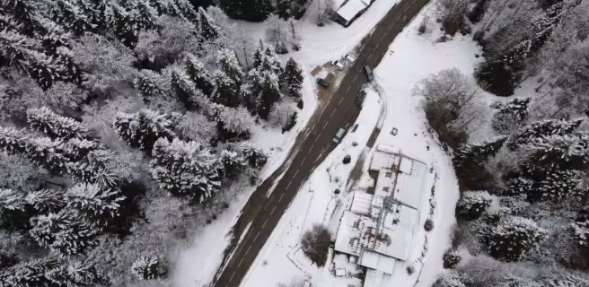 Vue drone du gîte et auberge de Carri à La Chapelle en Vercors, avec la route enneigée qui serpente à travers une forêt hivernale,.